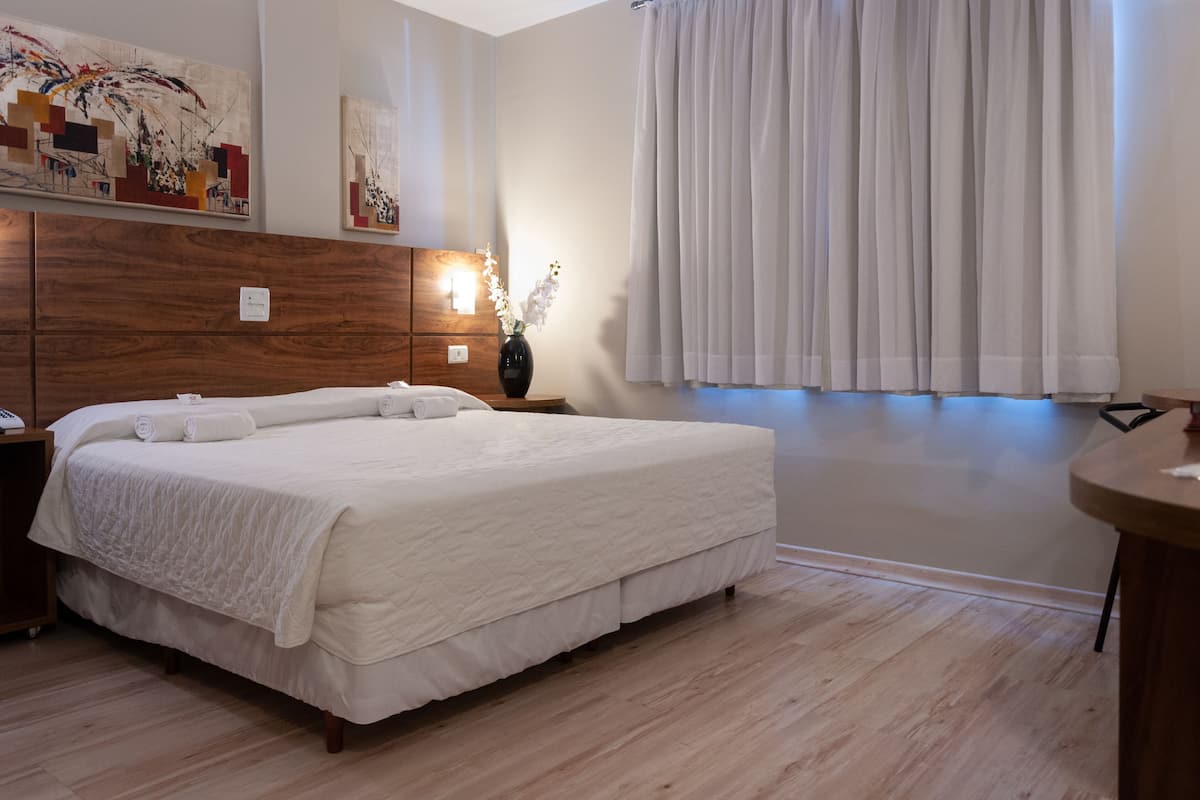Een net opgemaakt bed met witte linnens, een houten hoofdbord en een nachtkastje met een bloevas.