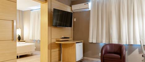 Una habitación de hotel moderna con una cama, un televisor montado en la pared, un refrigerador blanco pequeño y un sillón de cuero.