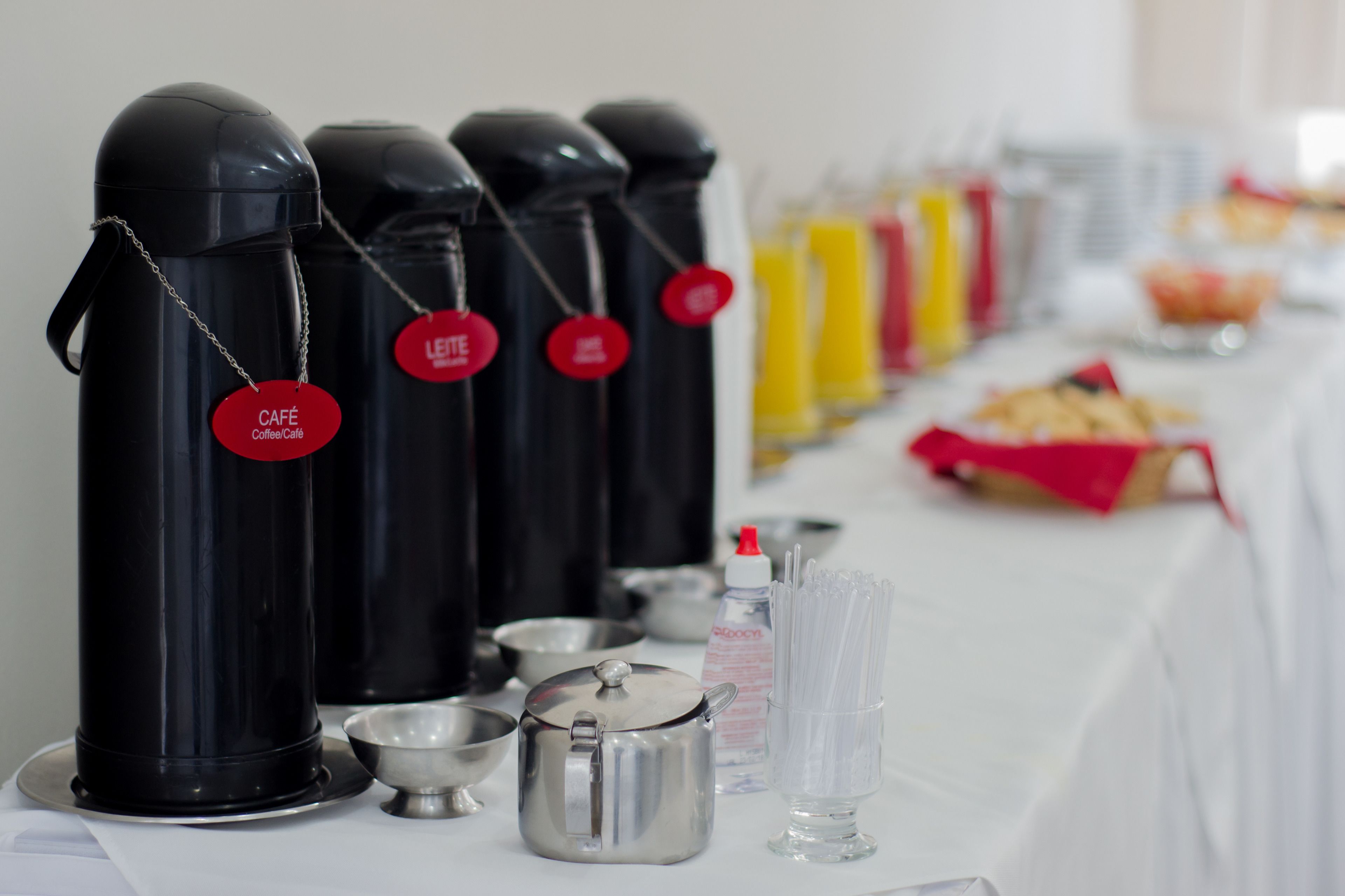 A buffet setup with black thermos cups labeled "Café Coffee Café" and a variety of food items on a white tablecloth.