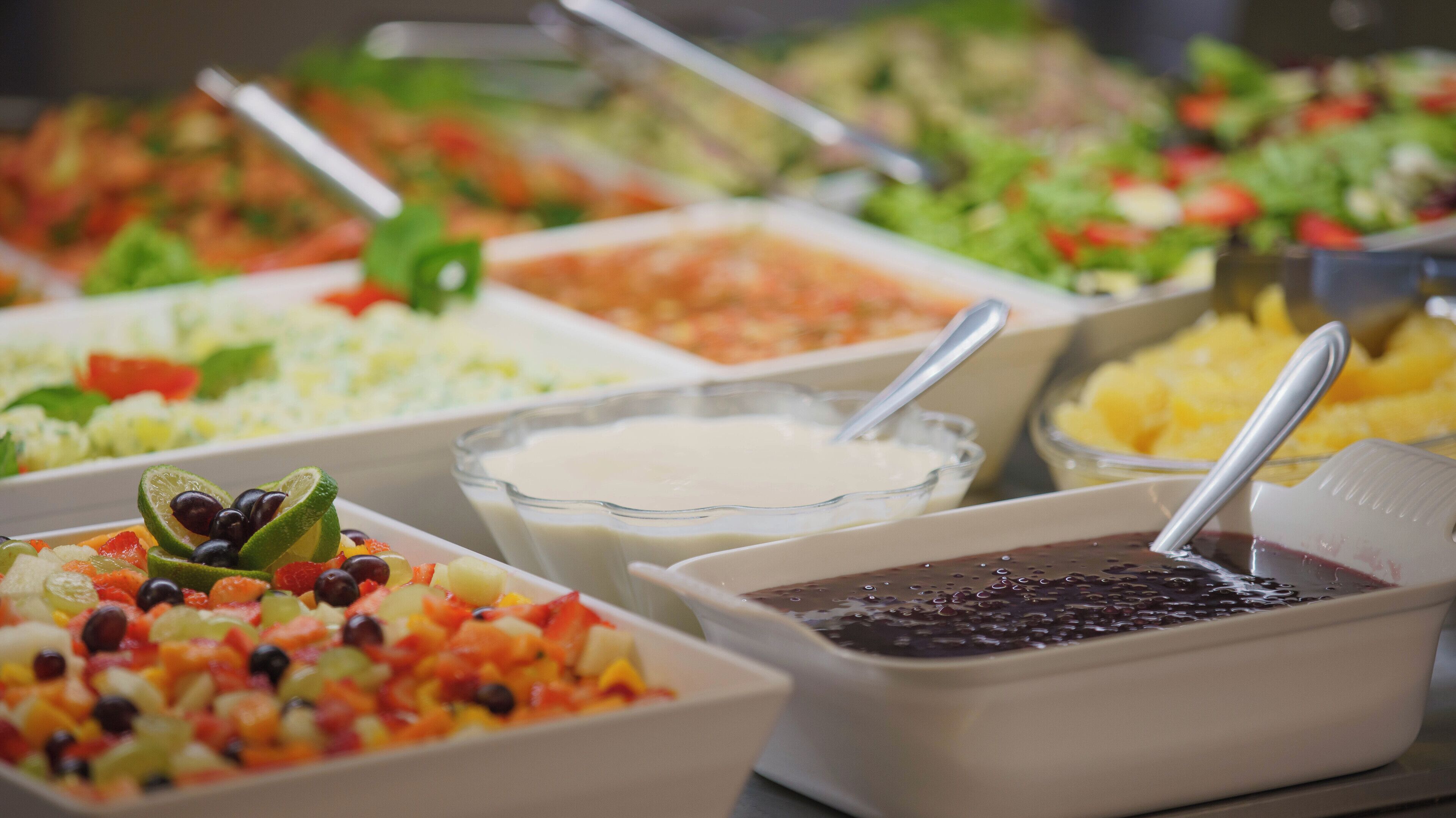 Un bufé con diversas opciones de comida, como ensaladas, frutas y salsas.
