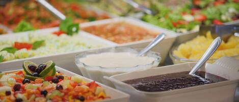 Un bufé con diversas opciones de comida, como ensaladas, frutas y salsas.