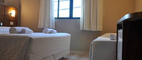 Une chambre d’hôtel avec deux lits, une fenêtre avec des rideaux, une tête de lit en bois et une petite table avec une lampe.