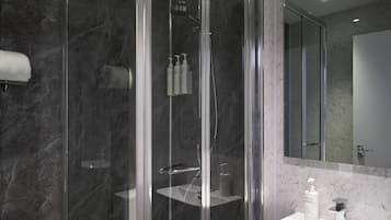 A modern bathroom with a glass-enclosed shower, a marble-tiled wall, a white sink, and a large mirror.