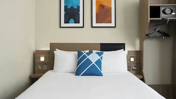 Habitación de hotel con cama, dos cuadros en la pared, un armario y un perchero.