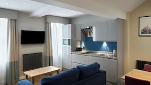 A modern kitchen with a built-in oven, a microwave, and a sink. There is a dining table and a blue sofa in the living area. - Four Points Flex by Sheraton Edinburgh (Edinburgh)