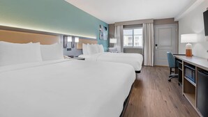 Habitación de hotel con dos camas, un escritorio, una silla, un televisor y una ventana con cortinas.