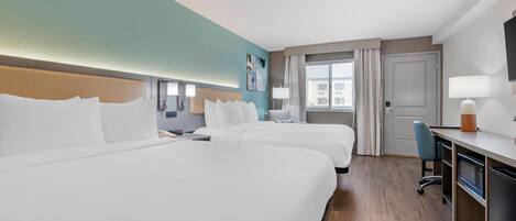 A hotel room with two beds, a desk, a chair, a TV, and a window with curtains.
