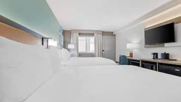 A hotel room with two beds, a TV, a desk with a lamp, and a window with curtains.