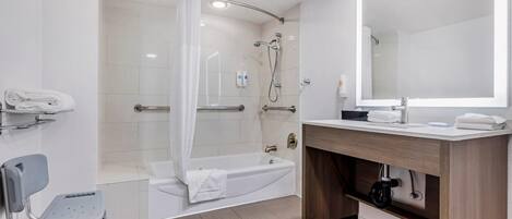 Un baño moderno con ducha, bañera, tocador con espejo y una silla accesible para silla de ruedas.