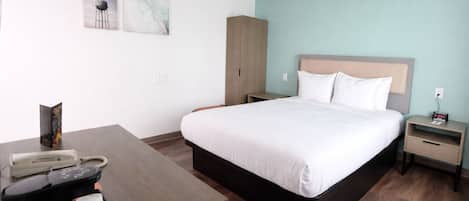 A hotel room with a bed, bedside tables, a desk with a telephone and coffee maker, and abstract wall art.