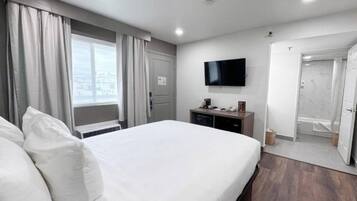A hotel room with a bed, a TV, a desk with a coffee machine, and a shower.