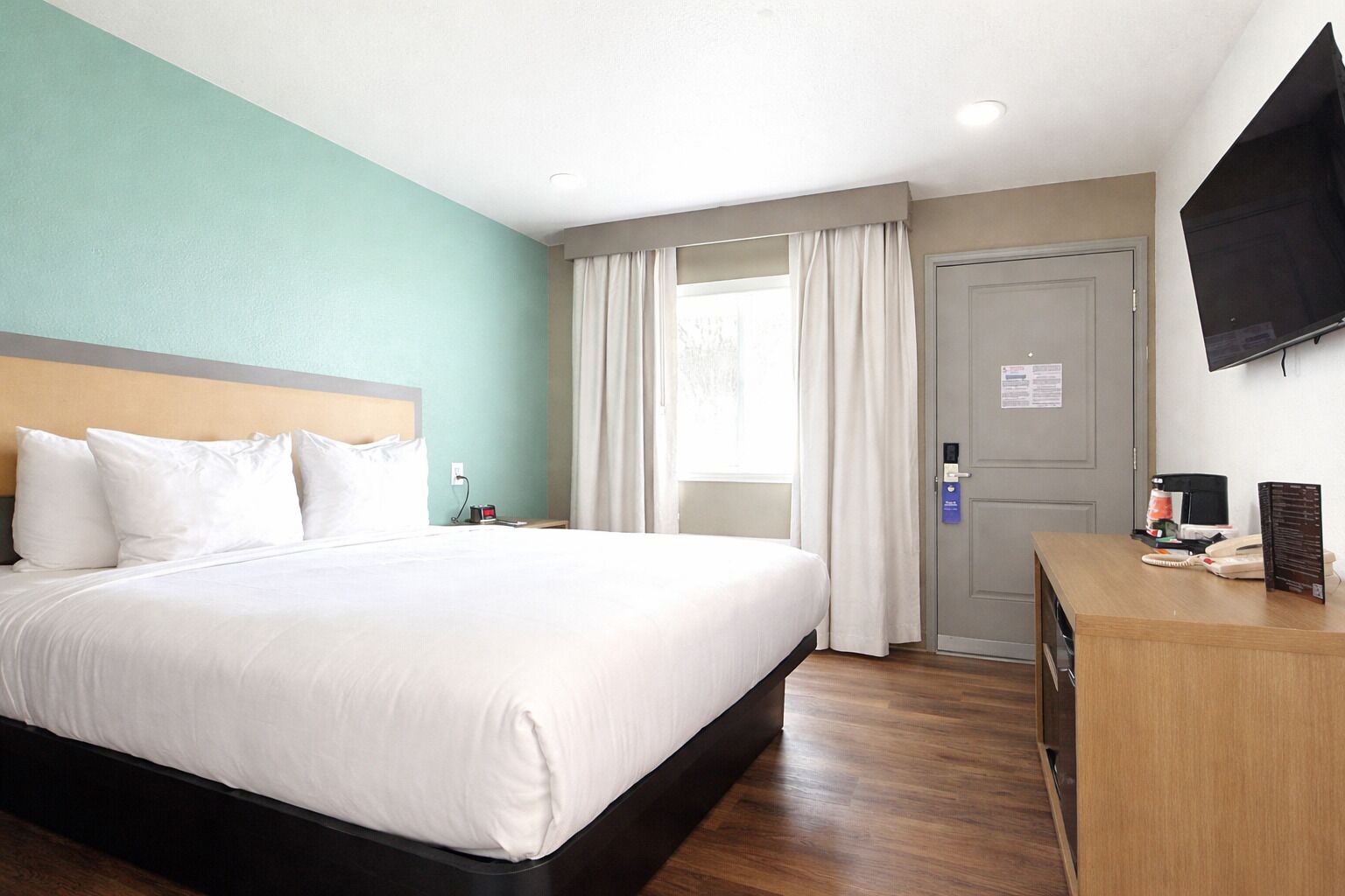 Une chambre d’hôtel avec un lit, un bureau doté d’un téléphone et d’un menu, un téléviseur fixé au mur et une porte avec une serrure.