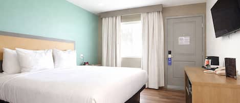 A hotel room with a bed, a desk with a phone and a menu, a TV on the wall, and a door with a lock.