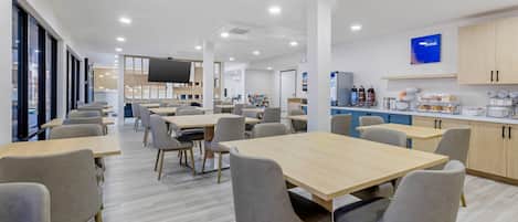 A modern dining area with tables and chairs, a kitchen area with cabinets and appliances, and a large window.