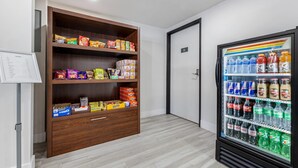 Una habitación con un armario de madera lleno de aperitivos y un refrigerador para bebidas.