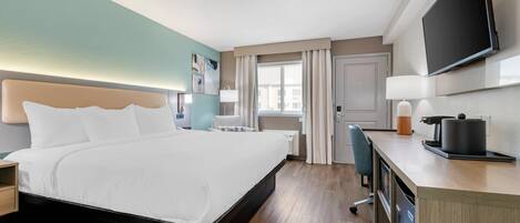 Habitación de hotel con cama, escritorio, televisor y ventana con cortinas.