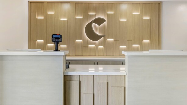 Un mostrador de recepción con un panel de pared de madera, un logo en forma de media luna y un terminal de pago digital.