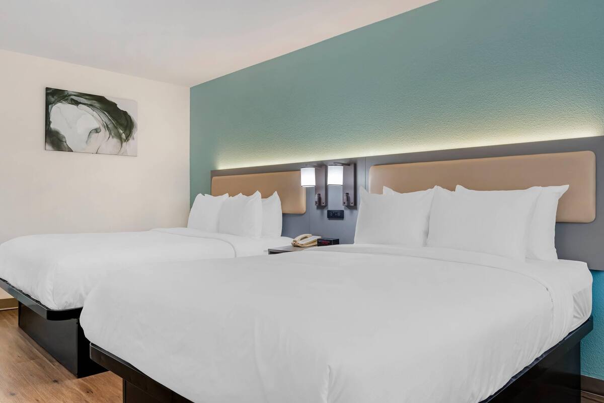 A hotel room with two beds, a painting on the wall, and a nightstand with a phone.