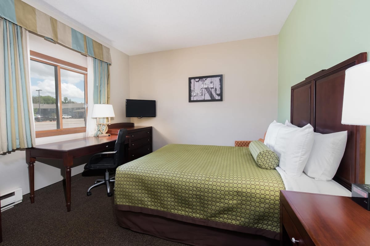A hotel room with a bed, desk, chair, TV, and a window with curtains.