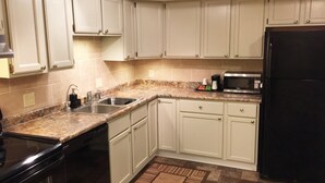A kitchen with white cabinets, a black refrigerator, a microwave, a sink, and a dishwasher. - Baymont by Wyndham Pierre (Pierre)