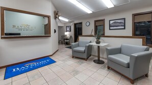 A reception area with a Baymont Inn & Suites sign, a reception desk, two grey armchairs, a small table with a plant, a clock, and framed pictures on the wall. - Baymont by Wyndham Pierre (Pierre)