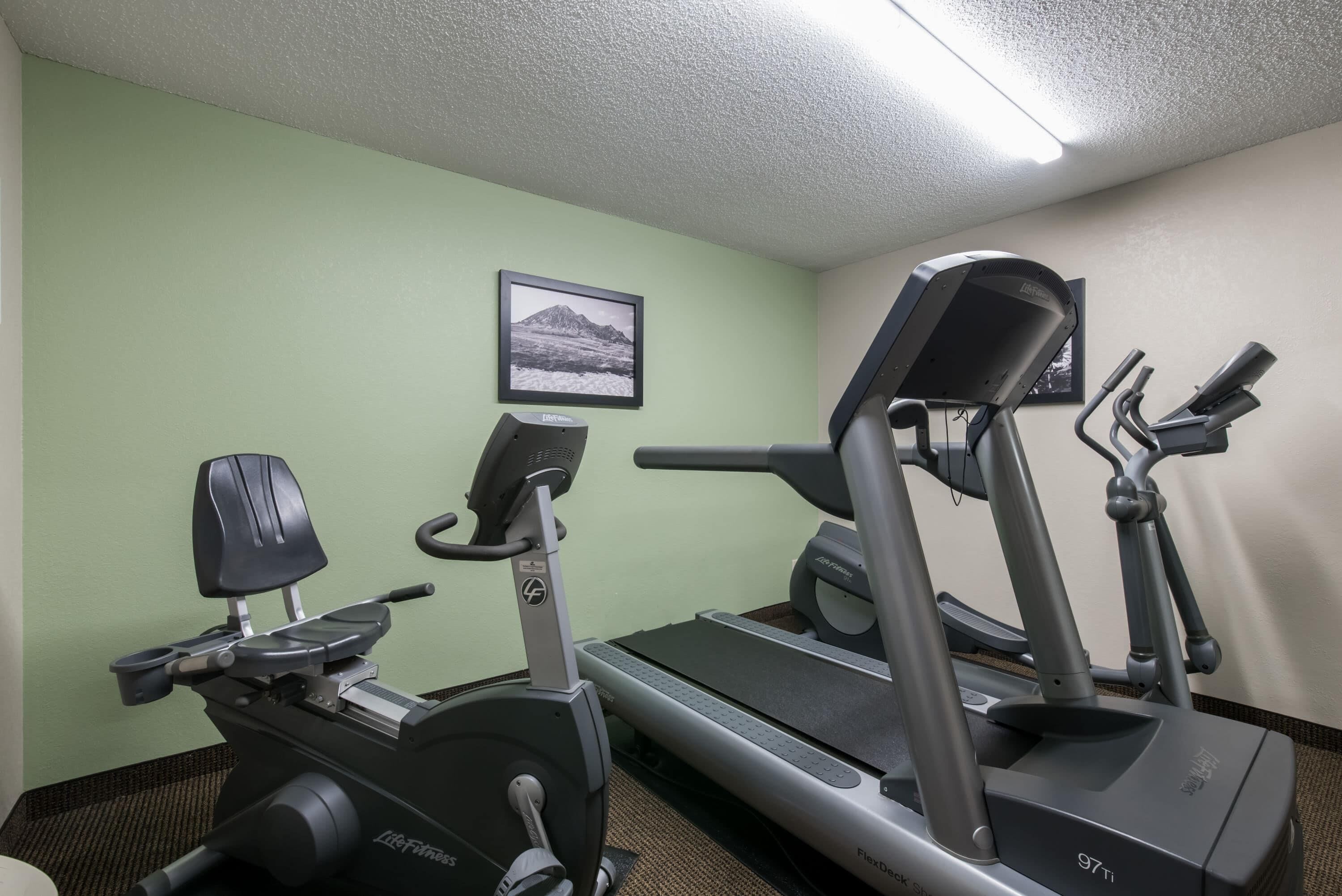 Un gimnasio con equipamiento cardiovascular, incluyendo una cinta de correr y una máquina elíptica.