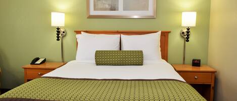 Quarto de hotel com uma cama grande, duas mesas de cabeceira com abajures, um quadro na parede e um edredom verde com padrão.