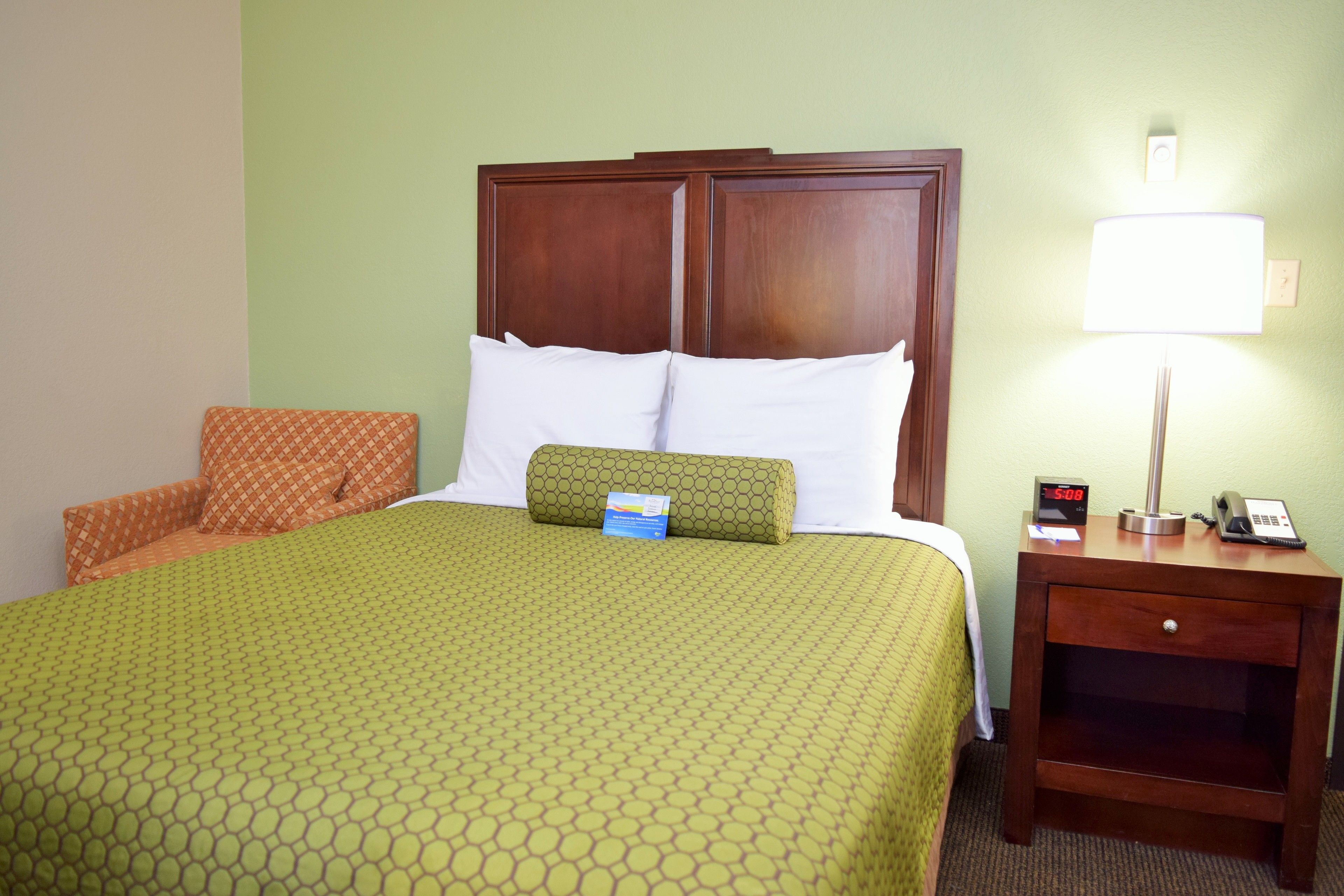 A hotel room with a bed, a nightstand with a lamp, and a clock.