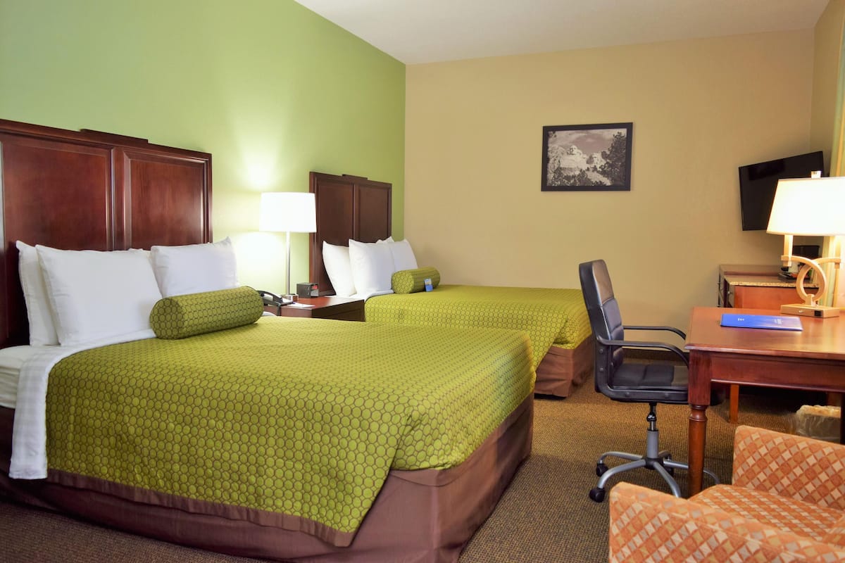 A hotel room with two beds, a desk, a chair, and a lamp.