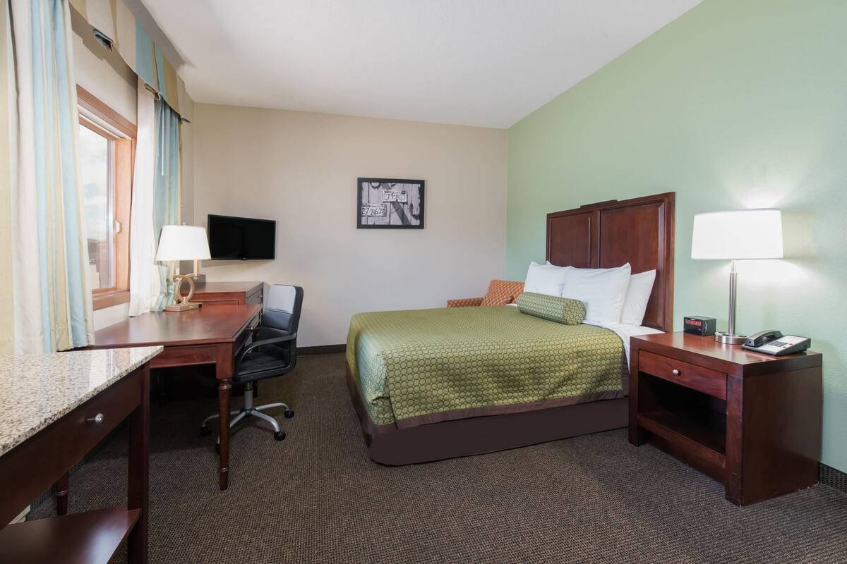 A hotel room with a bed, desk, chair, and a television on the wall.