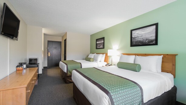A hotel room with two beds, a desk, a TV, and a framed picture on the wall. - Baymont by Wyndham Pierre (Pierre)