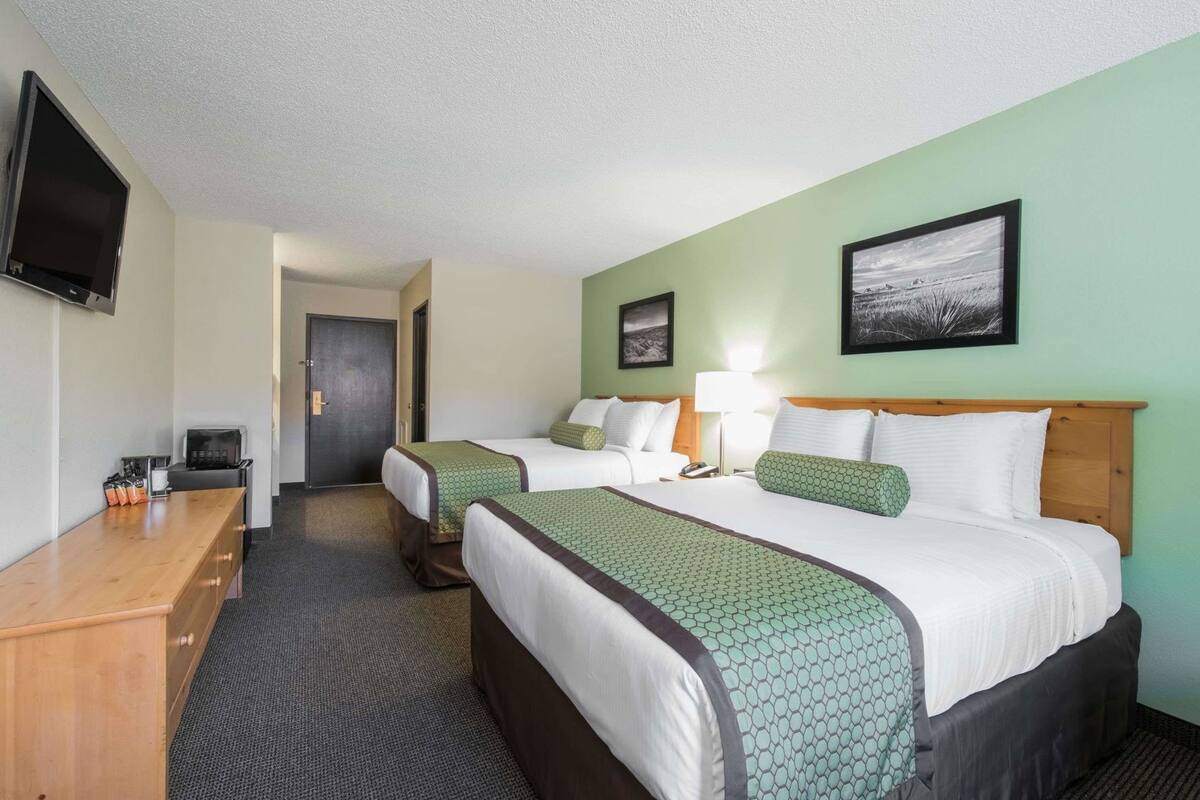 A hotel room with two beds, a desk, a TV, and a door.