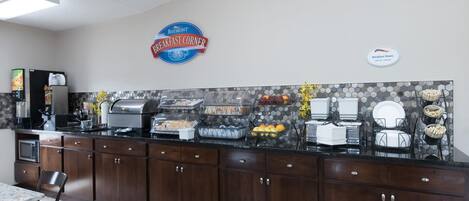 A breakfast buffet area with a Baymont Breakfast Corner sign, a microwave, and various breakfast items on the counter.