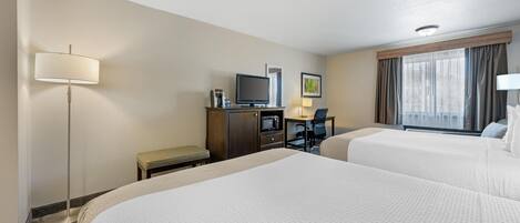 A hotel room with two beds, a desk with a computer, a flat-screen TV, a lamp, and a window with curtains.