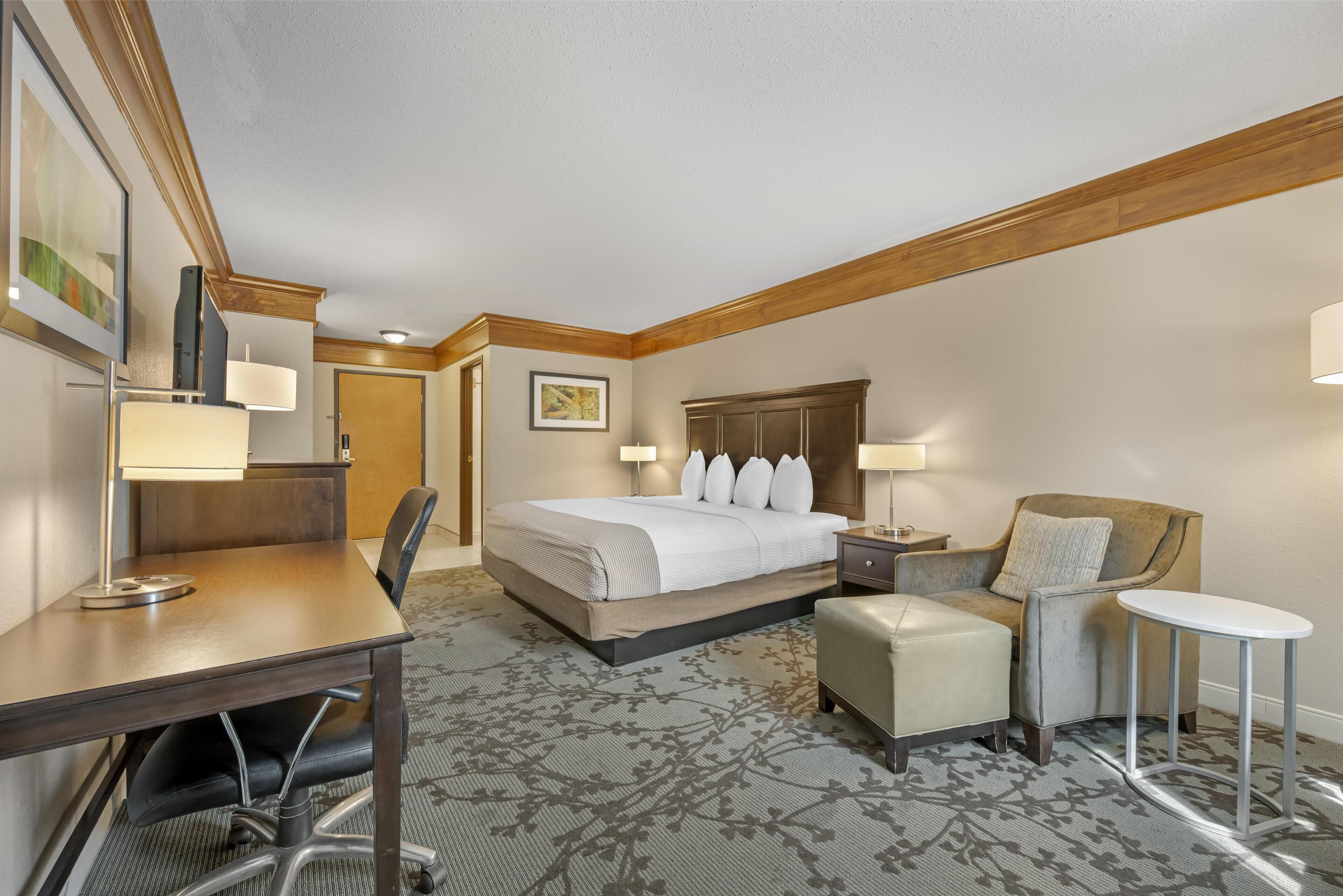 Une chambre d’hôtel avec un grand lit, un bureau, une chaise, une petite table et un canapé.