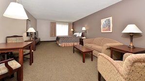 Una habitación de hotel con cama, dos sillones, un sofá, un escritorio y televisor.