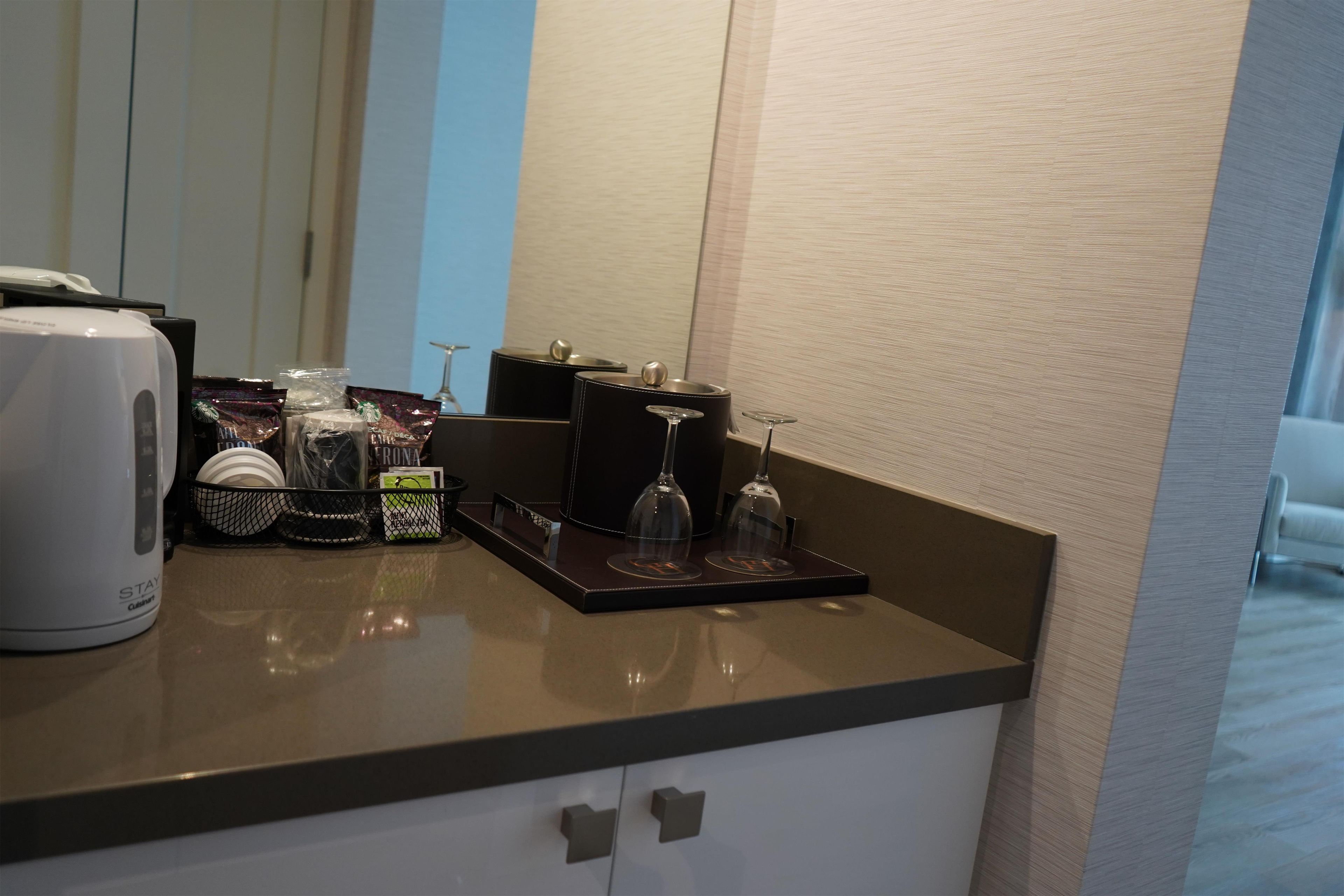 Un minibar in camera con una macchina per caffè, bicchieri da vino e prodotti a marchio Starbucks.
