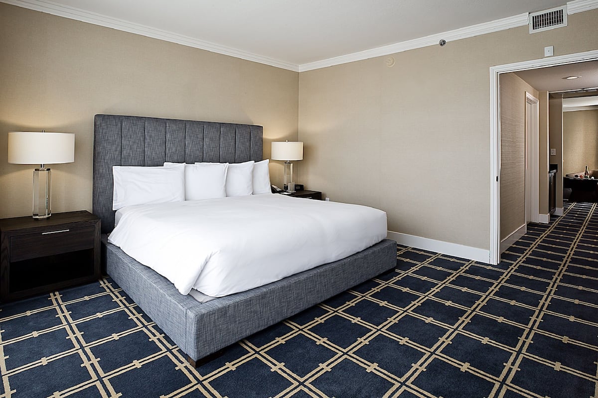 Una habitación de hotel con una cama grande, dos mesitas de noche y suelo alfombrado.