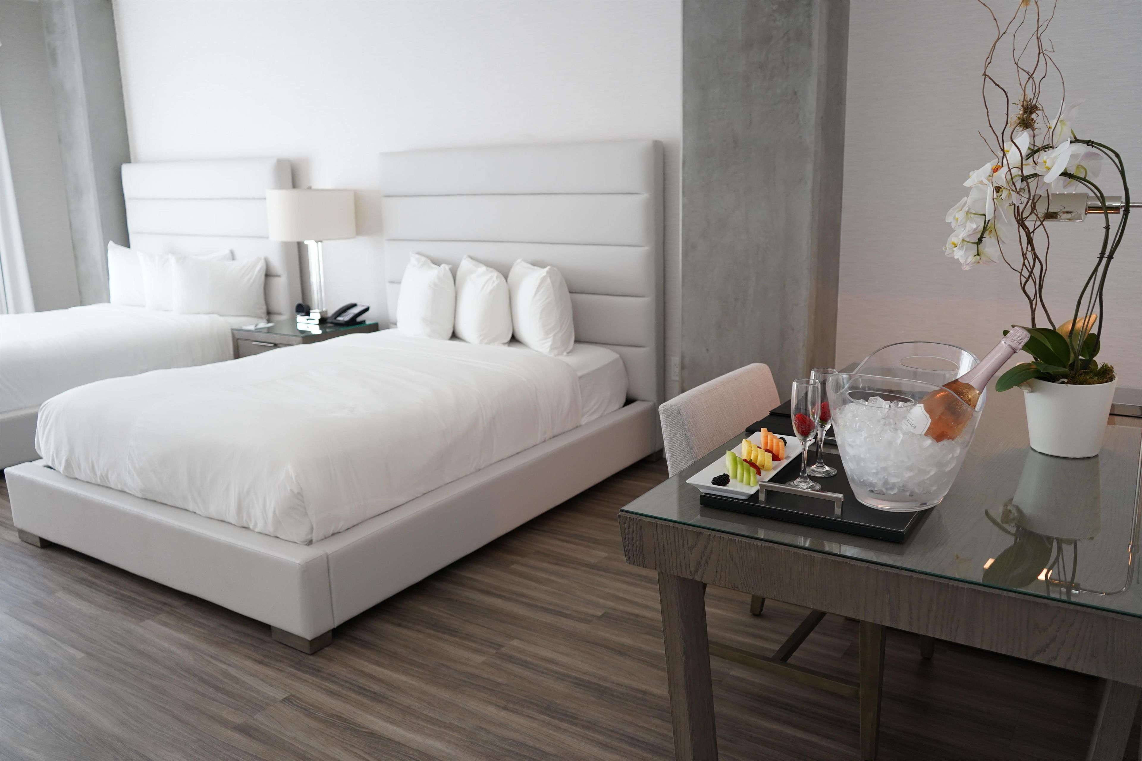 A modern hotel room with a large bed, a bedside table with a lamp, and a tray with fruit and ice.