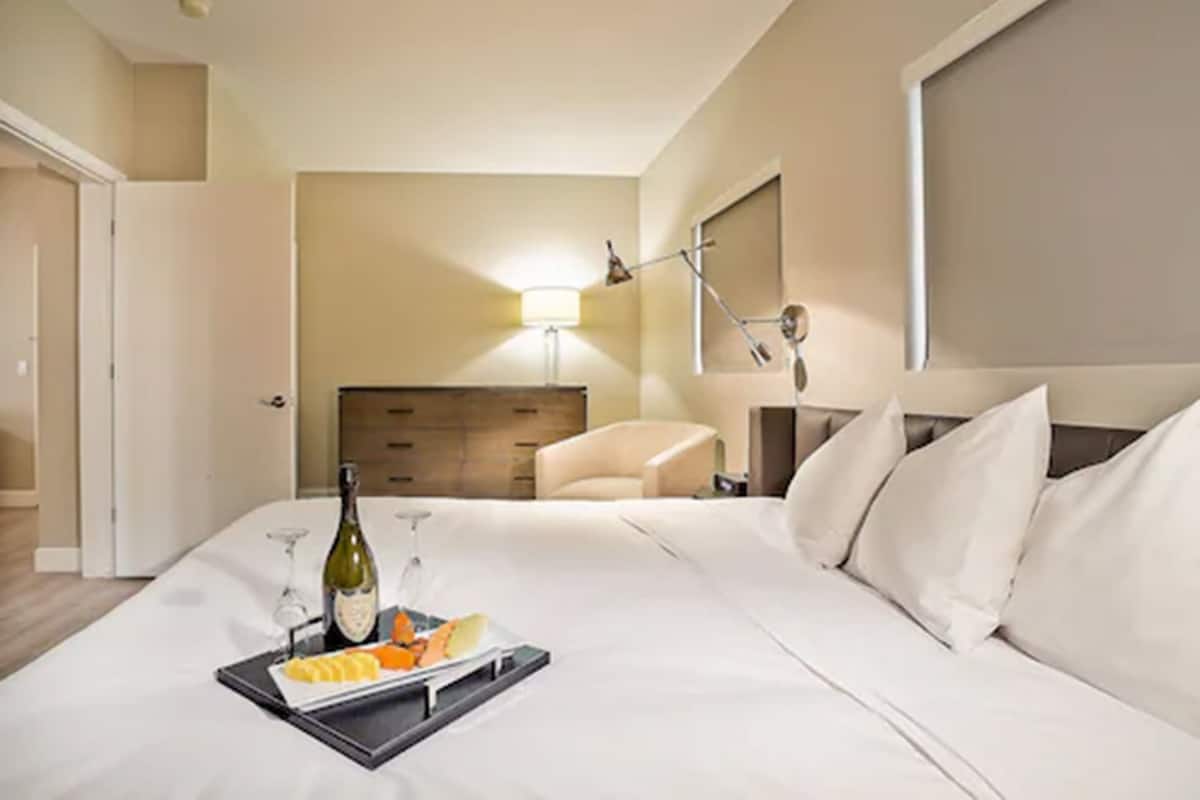 Habitación de hotel con cama, mesita de noche, lámpara, silla y bandeja con comida y bebidas.