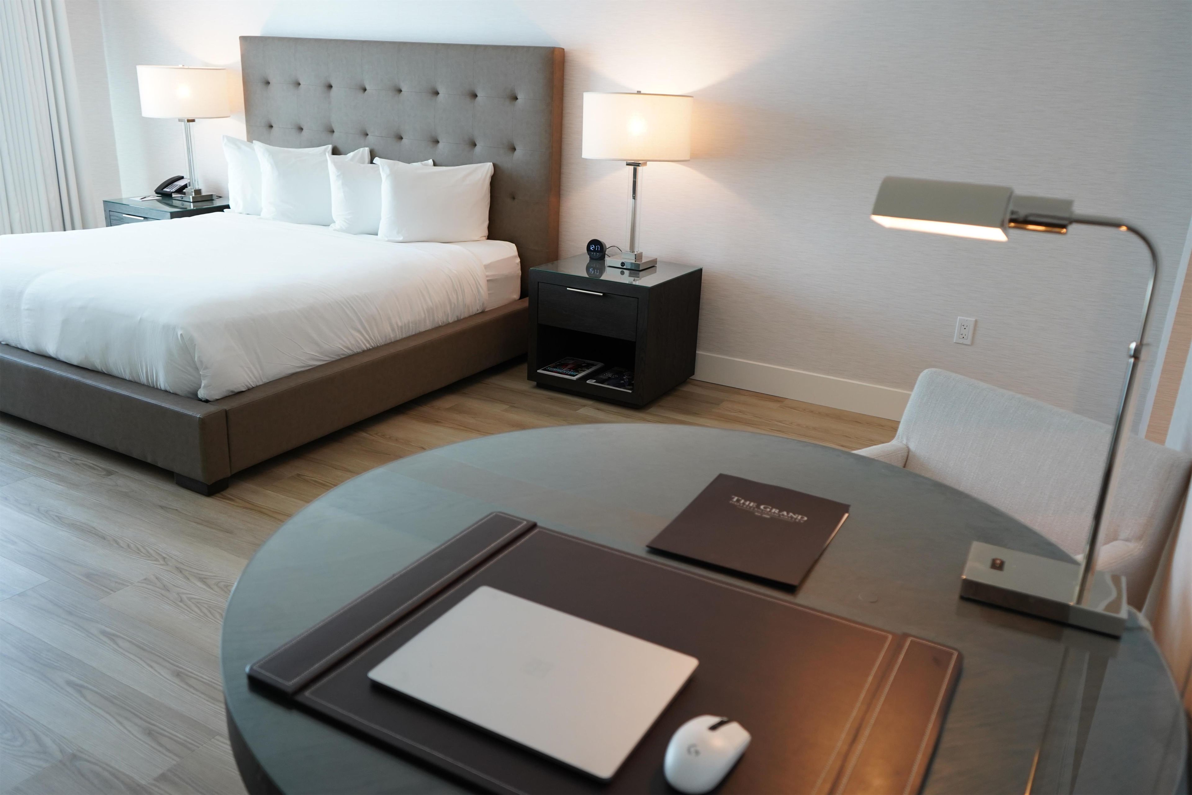 Une chambre d’hôtel comprenant un lit, des tables de chevet, un bureau avec une chaise, une lampe et un ordinateur.