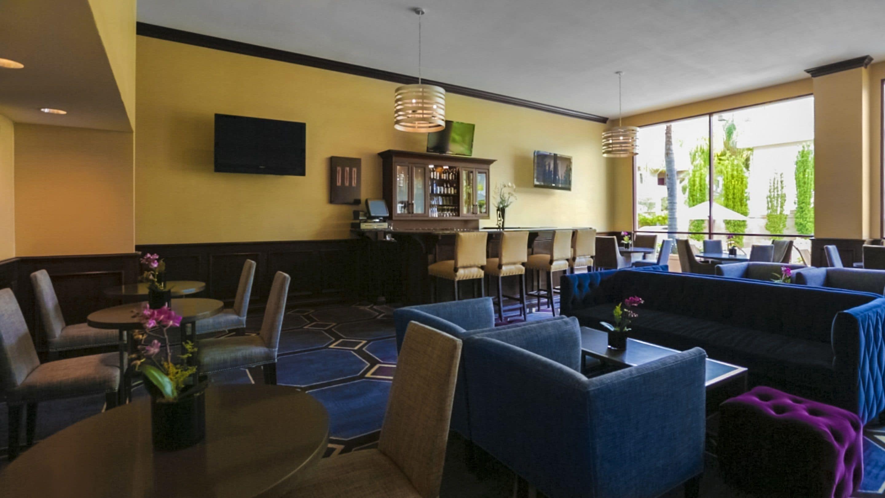 Un área de descanso moderna con asientos, un bar y grandes ventanales con vistas a zonas verdes.