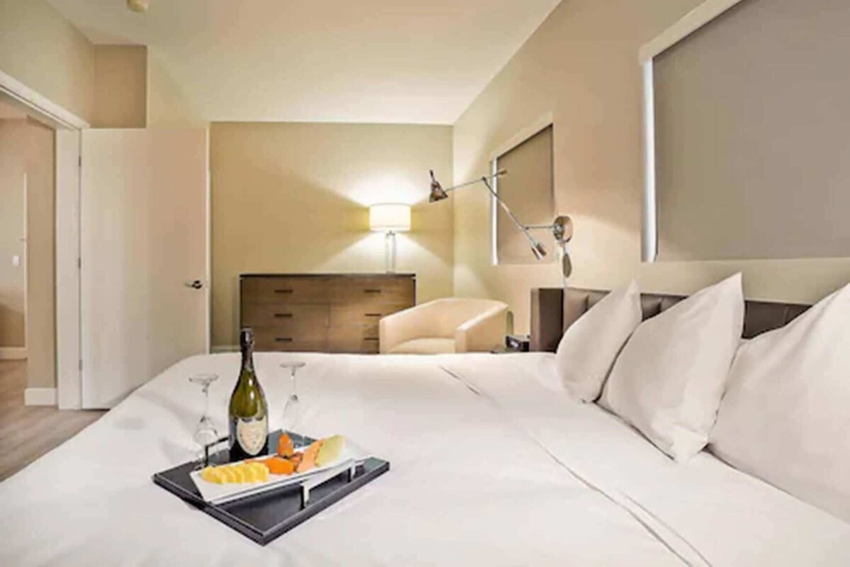 A hotel room with a bed, a bedside table with a tray of food and drinks, a lamp, and a chair.