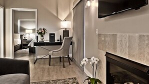 A modern living room with a fireplace, a dining area, and a kitchen in the background. - The Grand Hotel (Sunnyvale)