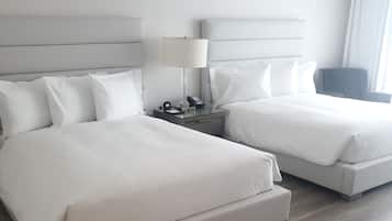 A hotel room with two beds, a bedside table with a lamp, and a chair.