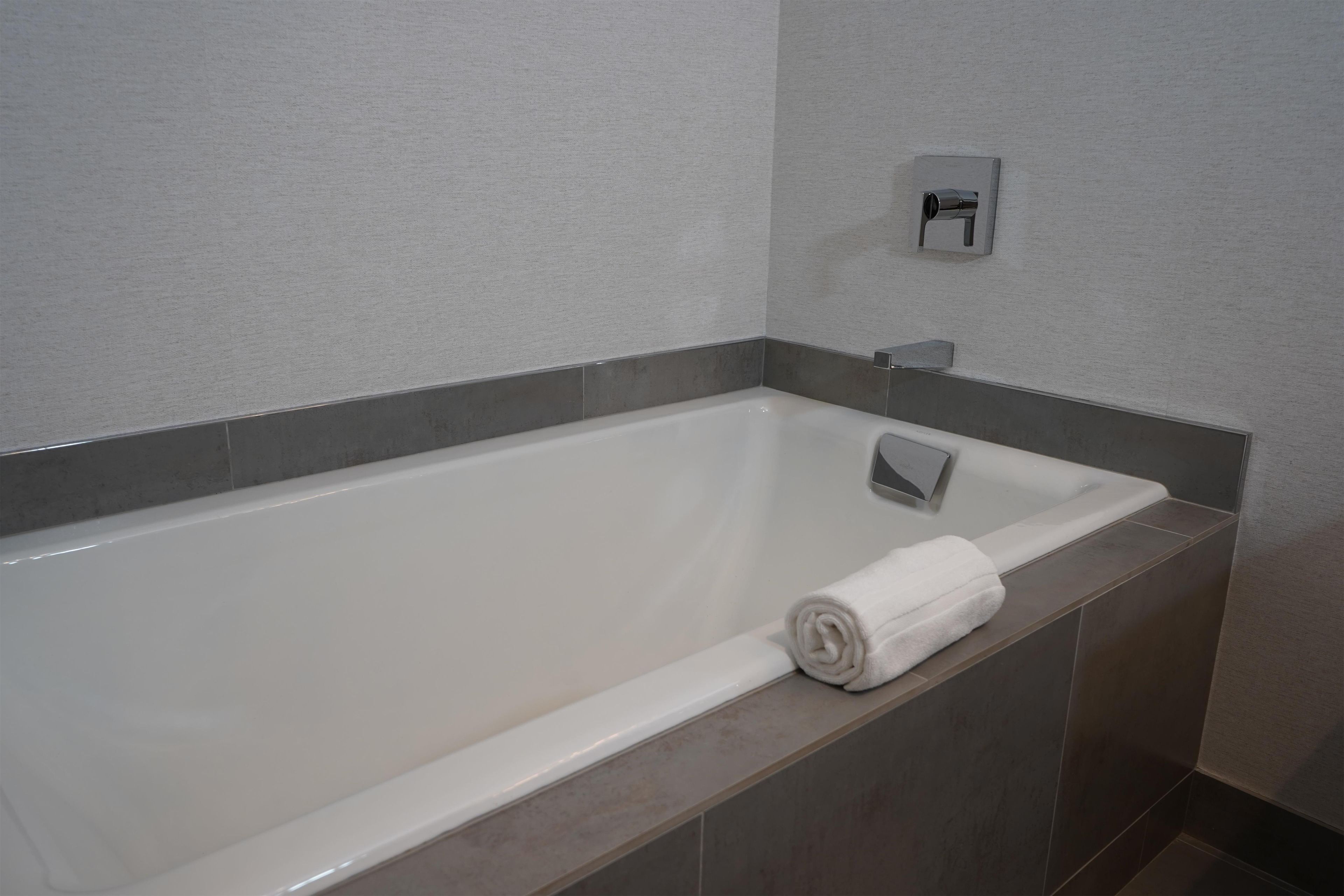A modern bathroom with a white bathtub, grey tiles, and a towel on the side.