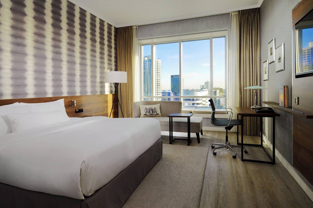 Una habitación de hotel con una cama grande, un escritorio, una silla y vistas del horizonte de la ciudad.