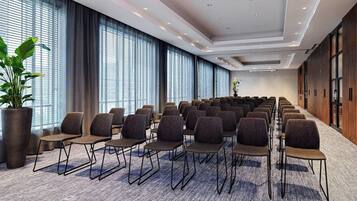 A conference room with rows of chairs, large windows, and a potted plant.