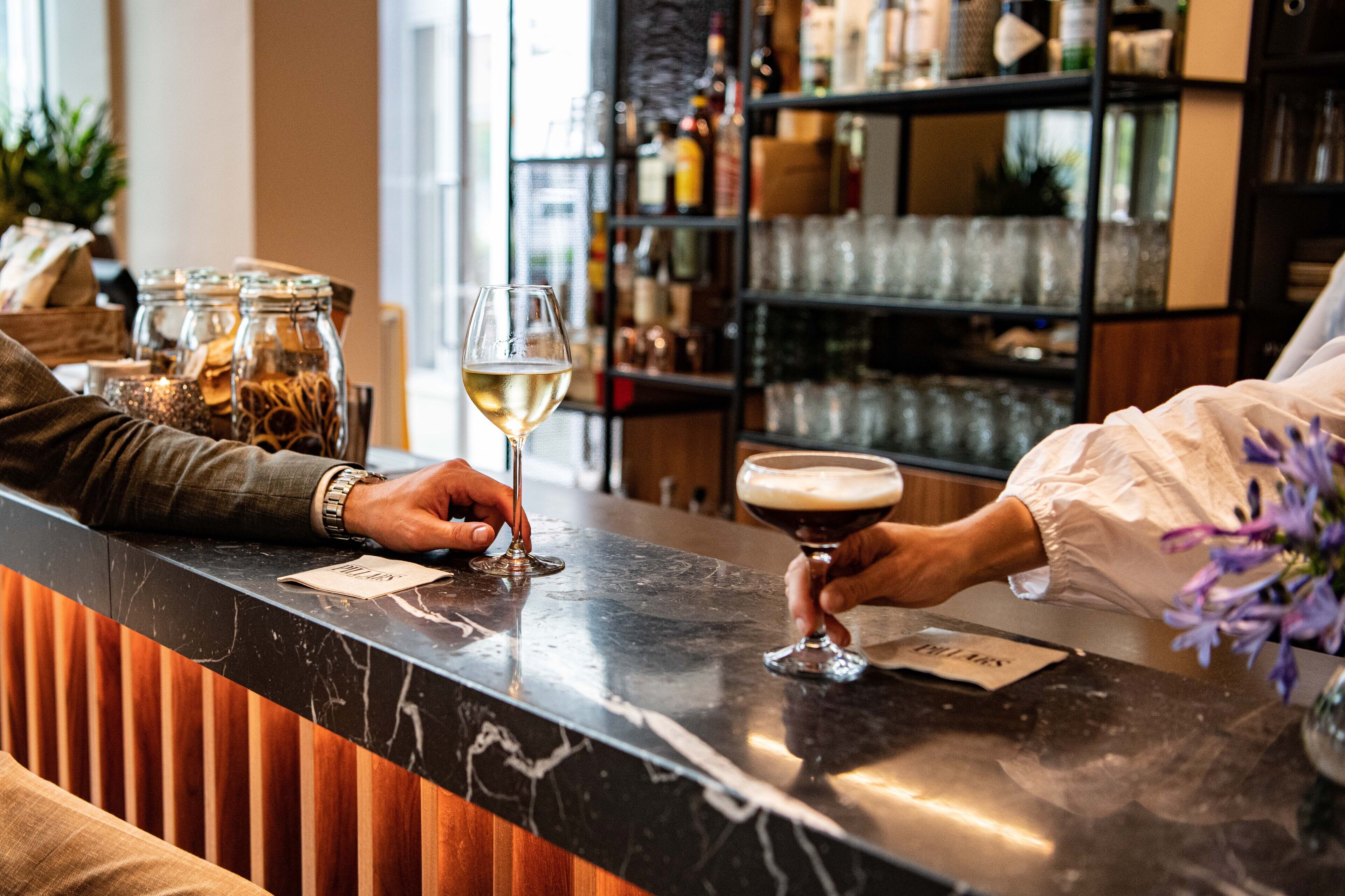 A bar area with a marble countertop, a wine glass, and a cocktail glass. There are jars with spices and a shelf with bottles in the background.