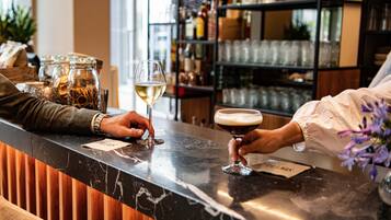 A bar area with a marble countertop, a wine glass, and a cocktail glass. There are jars with spices and a shelf with bottles in the background.